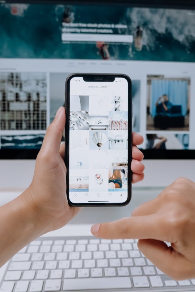 person-holding-white-samsung-galaxy-smartphone-5082578 Person using smartphone to browse photos, office desktop setup.